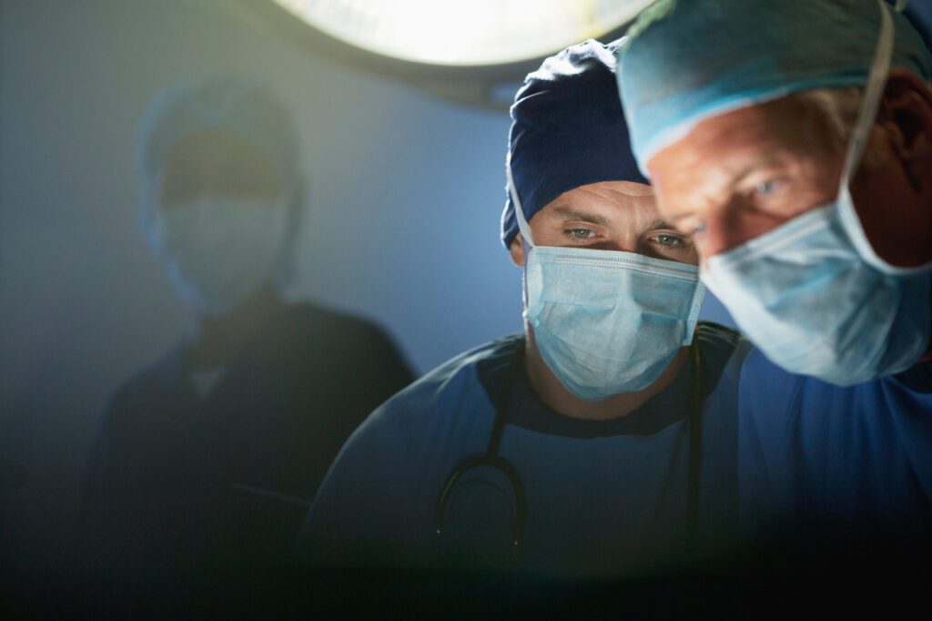 Nahaufnahme von zwei Operateuren mit Mundschutz und Haube im Operationssaal