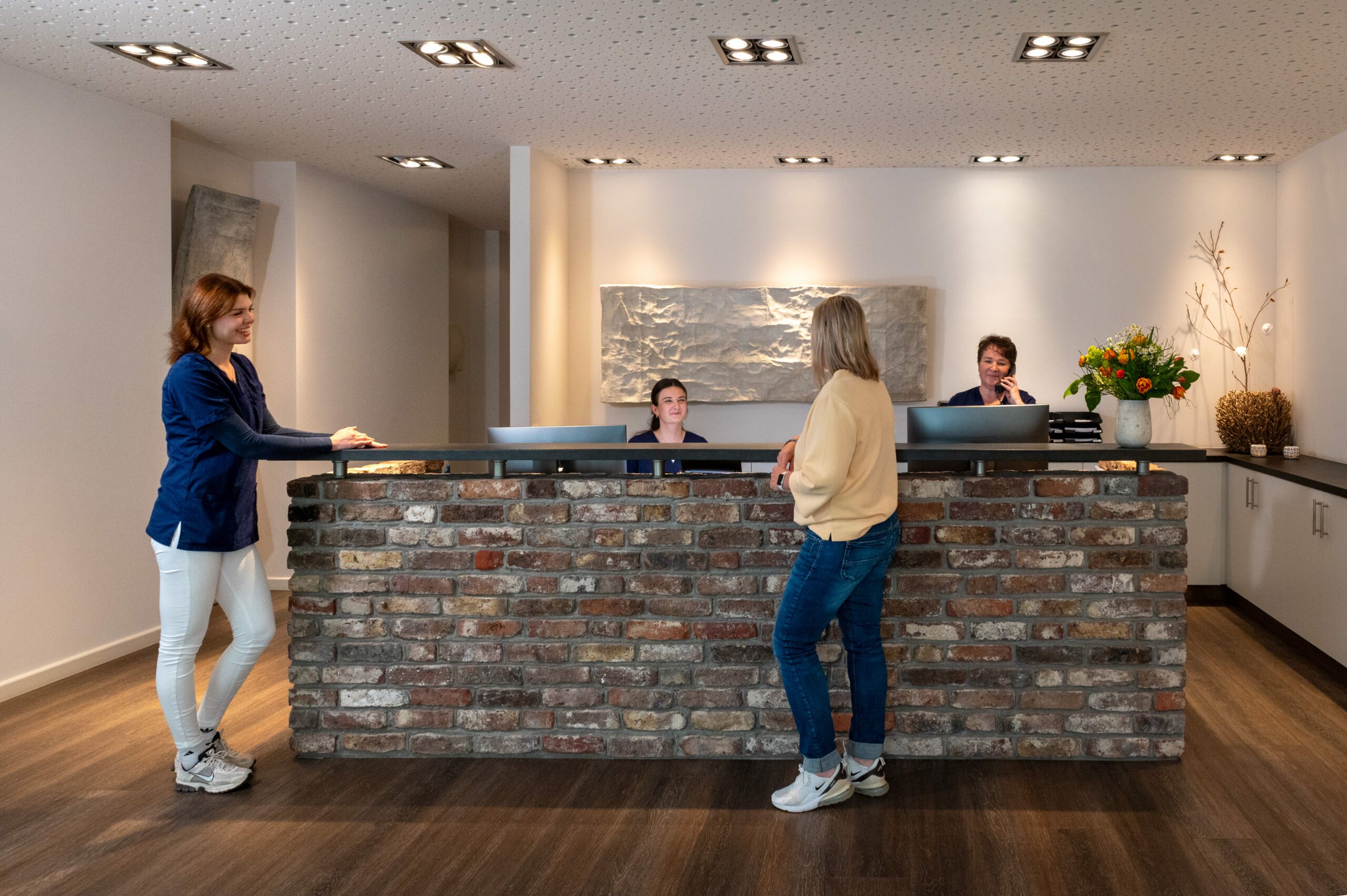 Empfangsbereich des radiologischen Standorts in Deutz mit freundlichem mamonova-Team. Zwei Mitarbeiterinnen stehen im Austausch mit einer Patientin, eine weitere telefoniert am Tresen.